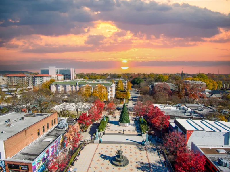 an aerial shot of the Decatur Square with a Christmas tree, red and yellow autumn trees, lush green trees, people and buildings with powerful clouds at sunset in Decatur Georgia USA